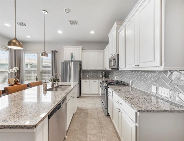 17023 Canosa Dr, Cypress, TX 77433 - kitchen with appliances with stainless steel finishes, white cabinetry, decorative backsplash, a center island with sink, and decorative light fixtures