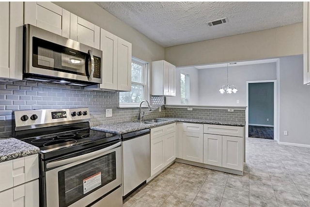 4137 Galesburg St, Houston, TX 77051 - kitchen with stainless steel appliances, white cabinets, a chandelier, stone counters, and a textured ceiling