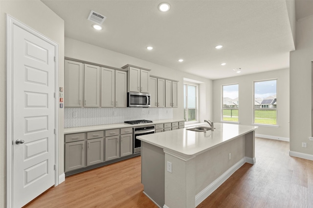6322 Cambrai Wood Ln, Katy, TX 77493 - kitchen with appliances with stainless steel finishes, gray cabinetry, light wood-style floors, a kitchen island with sink, and recessed lighting