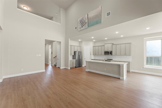 6322 Cambrai Wood Ln, Katy, TX 77493 - kitchen with appliances with stainless steel finishes, light countertops, light wood-style floors, an island with sink, and open floor plan