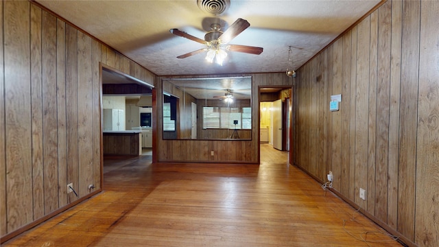 6619 Heron Dr, Houston, TX 77087 - unfurnished living room with light wood finished floors, wood walls, ceiling fan, and a textured ceiling