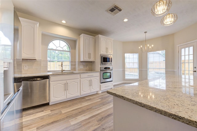 22934 Cove Timbers Ct, Tomball, TX 77375 - kitchen featuring appliances with stainless steel finishes, a chandelier, white cabinets, light wood-style flooring, and light stone counters