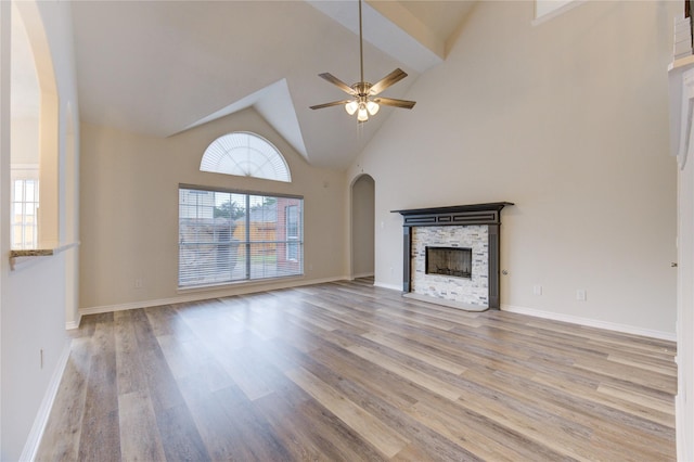22934 Cove Timbers Ct, Tomball, TX 77375 - unfurnished living room featuring a stone fireplace, arched walkways, light wood-style floors, a ceiling fan, and high vaulted ceiling
