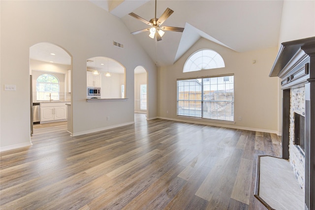 22934 Cove Timbers Ct, Tomball, TX 77375 - unfurnished living room with ceiling fan, wood finished floors, a stone fireplace, high vaulted ceiling, and arched walkways