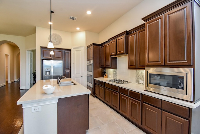 19750 Lago Terrace Loop, Richmond, TX 77407 - kitchen featuring appliances with stainless steel finishes, arched walkways, light countertops, dark brown cabinets, and decorative backsplash