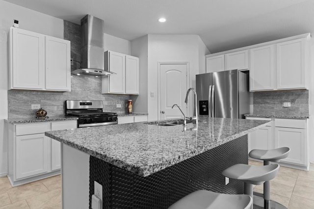 14205 Dream Rd, New Caney, TX 77357 - kitchen featuring appliances with stainless steel finishes, wall chimney range hood, light stone counters, a kitchen island with sink, and a breakfast bar area