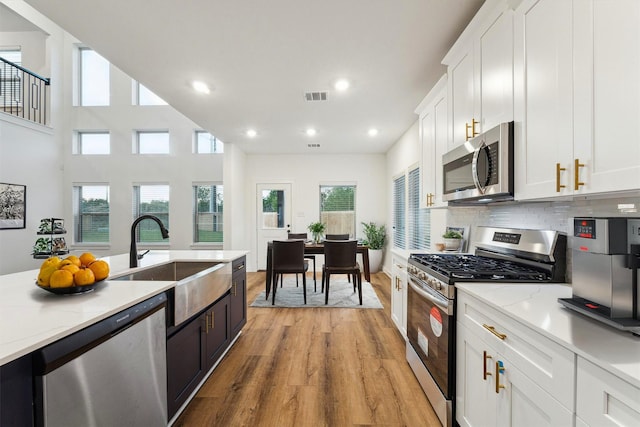 390 Kendall Crest Dr, Alvin, TX 77511 - kitchen with stainless steel appliances, light wood-style floors, white cabinetry, recessed lighting, and backsplash
