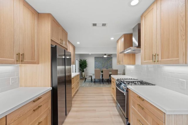 4406 Merwin St, Houston, TX 77027 - kitchen featuring stainless steel range with gas stovetop, freestanding refrigerator, wall chimney exhaust hood, light brown cabinets, and recessed lighting