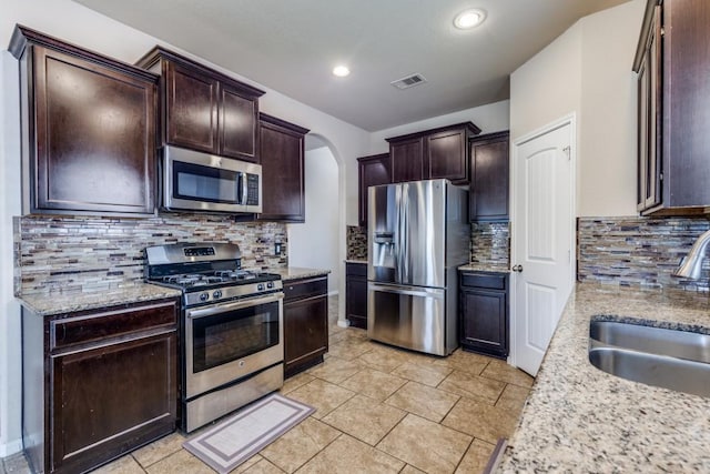 23606 Stargazer Pt, Spring, TX 77373 - kitchen with stainless steel appliances, arched walkways, tasteful backsplash, dark brown cabinets, and light stone counters