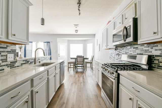 2526 Hidden Park Ln, Conroe, TX 77385 - kitchen with stainless steel appliances, backsplash, light wood finished floors, light countertops, and decorative light fixtures
