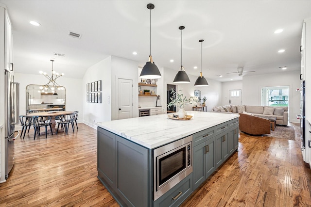 1247 Martin St, Houston, TX 77018 - kitchen featuring gray cabinetry, stainless steel microwave, light wood-style floors, a center island, and light stone counters