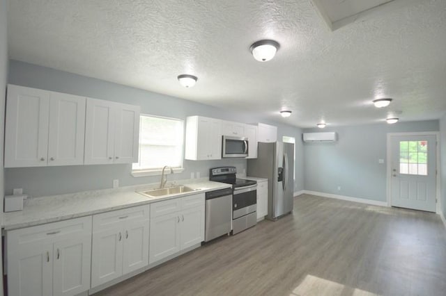 3007 Tuam St, Houston, TX 77004 - kitchen featuring stainless steel appliances, a wall mounted AC, white cabinetry, light wood-style flooring, and a textured ceiling