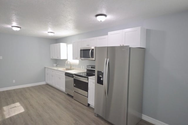 3007 Tuam St, Houston, TX 77004 - kitchen with appliances with stainless steel finishes, white cabinetry, a textured ceiling, light wood finished floors, and light countertops