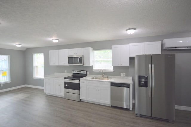 3007 Tuam St, Houston, TX 77004 - kitchen featuring appliances with stainless steel finishes, a wall unit AC, a textured ceiling, white cabinets, and wood finished floors