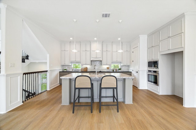 306 Felt Cir, Houston, TX 77011 - kitchen with appliances with stainless steel finishes, a kitchen island with sink, light wood-style flooring, recessed lighting, and a kitchen breakfast bar