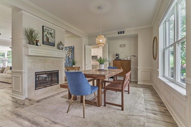 22811 Northampton Pines Dr, Spring, TX 77389 - dining space with crown molding, a tiled fireplace, light wood finished floors, wainscoting, and a decorative wall