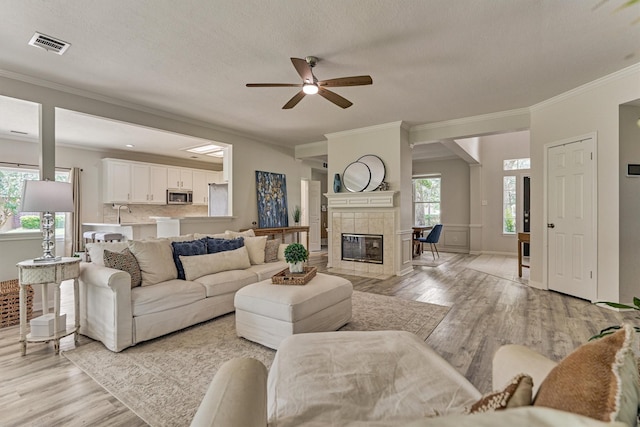 22811 Northampton Pines Dr, Spring, TX 77389 - living room featuring light wood-style floors, a ceiling fan, ornamental molding, plenty of natural light, and a tiled fireplace
