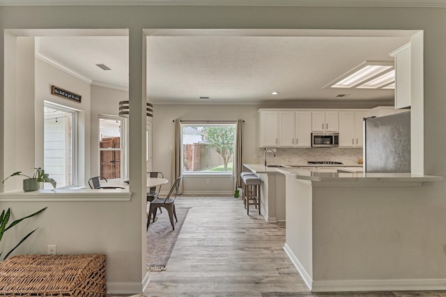 22811 Northampton Pines Dr, Spring, TX 77389 - kitchen with stainless steel appliances, crown molding, light wood-style floors, white cabinetry, and backsplash
