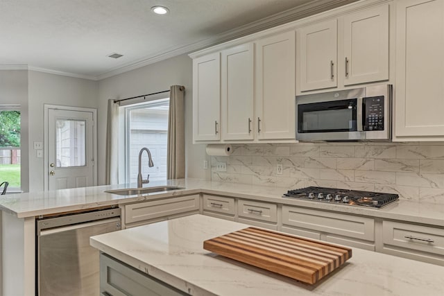 22811 Northampton Pines Dr, Spring, TX 77389 - kitchen featuring appliances with stainless steel finishes, a peninsula, white cabinetry, backsplash, and crown molding