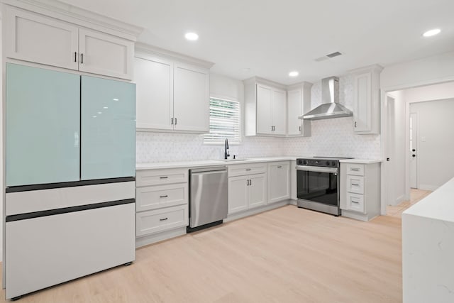 8215 Twining Oaks Ln, Spring, TX 77379 - kitchen with wall chimney range hood, appliances with stainless steel finishes, light wood-style floors, tasteful backsplash, and light countertops