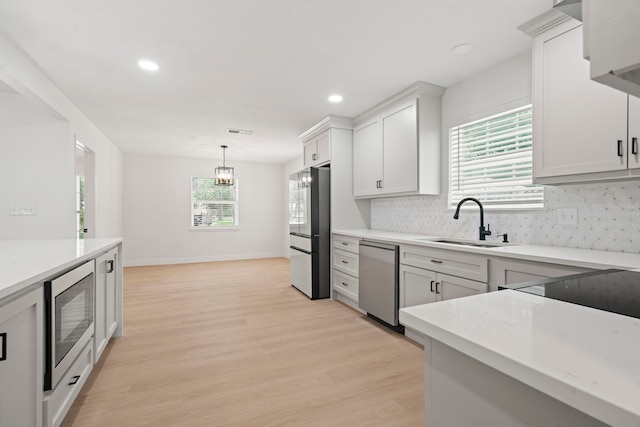 8215 Twining Oaks Ln, Spring, TX 77379 - kitchen featuring appliances with stainless steel finishes, light wood-style flooring, decorative backsplash, pendant lighting, and white cabinetry