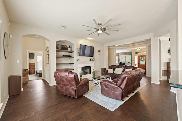 18114 Rustic Springs Dr, Tomball, TX 77375 - living room featuring ceiling fan, dark wood-style flooring, a fireplace, arched walkways, and built in features