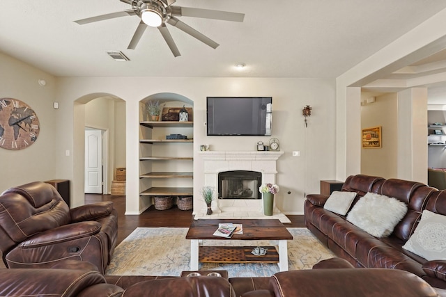 18114 Rustic Springs Dr, Tomball, TX 77375 - living room featuring a ceiling fan, wood finished floors, a fireplace, built in features, and arched walkways