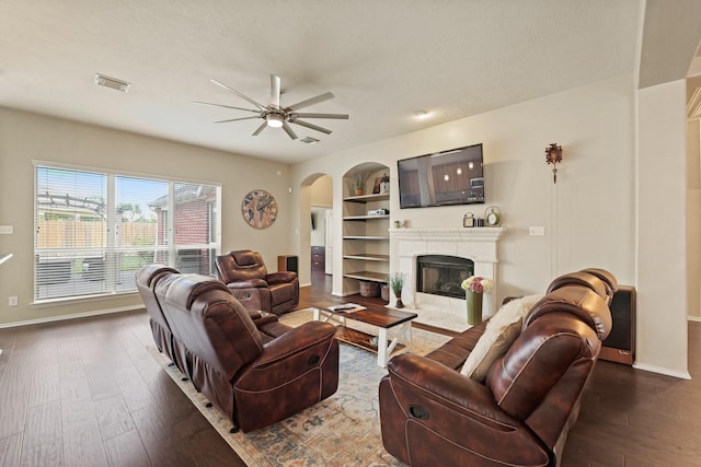 18114 Rustic Springs Dr, Tomball, TX 77375 - living room with arched walkways, a ceiling fan, dark wood-style floors, built in shelves, and a fireplace