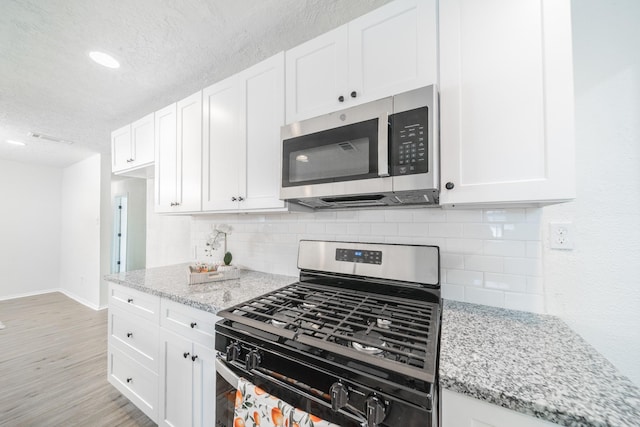8318 Hanfro Ln, Houston, TX 77088 - kitchen with stainless steel appliances, a textured ceiling, white cabinetry, backsplash, and light stone countertops