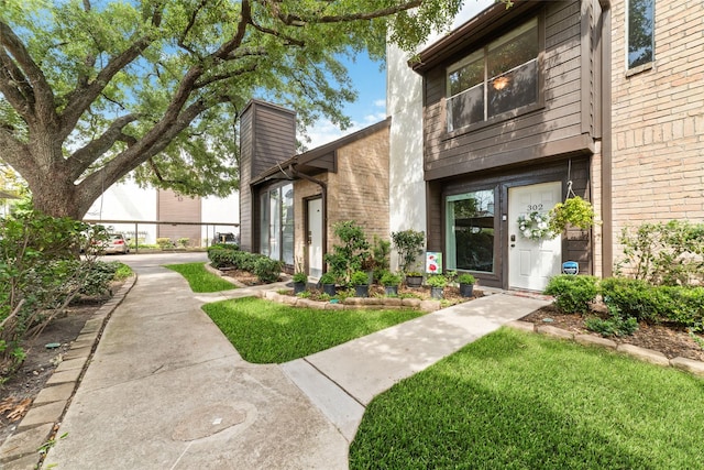 2601 S Braeswood Blvd Unit 302, Houston, TX 77025 - doorway to property featuring a chimney, brick siding, and a yard