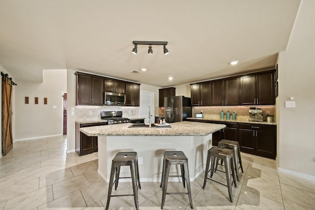 29023 Jacobs River Dr, Katy, TX 77494 - kitchen with appliances with stainless steel finishes, tasteful backsplash, a kitchen bar, a barn door, and a center island with sink