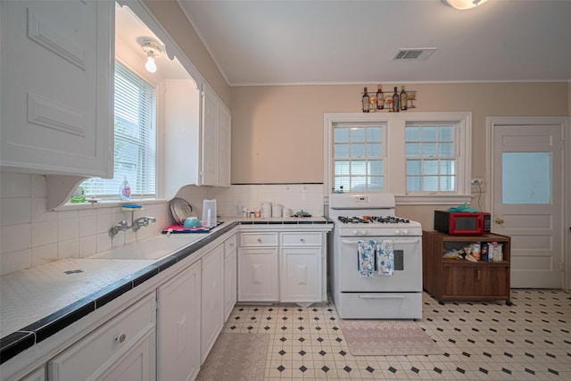 604 Abell St, Wharton, TX 77488 - kitchen featuring white gas stove, white cabinetry, light floors, crown molding, and tile countertops