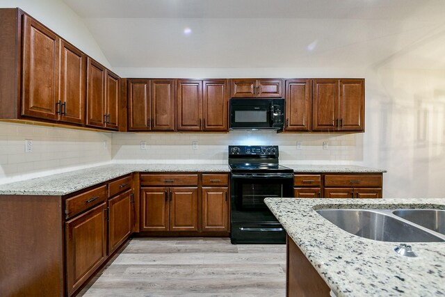 167 Courageous Side Way, Magnolia, TX 77354 - kitchen with black appliances, light stone counters, light wood-style floors, decorative backsplash, and vaulted ceiling