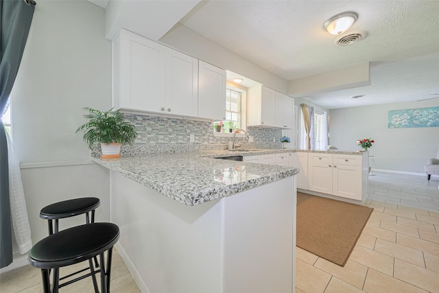 101 Wildrose St, Baytown, TX 77520 - kitchen featuring a peninsula, white cabinets, tasteful backsplash, light stone countertops, and wainscoting