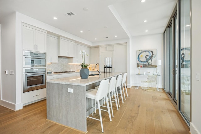 5656 San Felipe St Unit 606, Houston, TX 77056 - kitchen featuring light wood finished floors, a center island with sink, tasteful backsplash, a breakfast bar, and appliances with stainless steel finishes