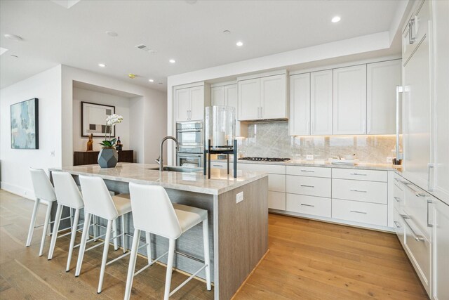 5656 San Felipe St Unit 606, Houston, TX 77056 - kitchen featuring a kitchen island with sink, tasteful backsplash, light wood-type flooring, light stone counters, and recessed lighting
