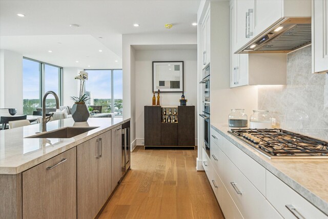 5656 San Felipe St Unit 606, Houston, TX 77056 - kitchen featuring stainless steel appliances, custom range hood, light wood-type flooring, backsplash, and white cabinets