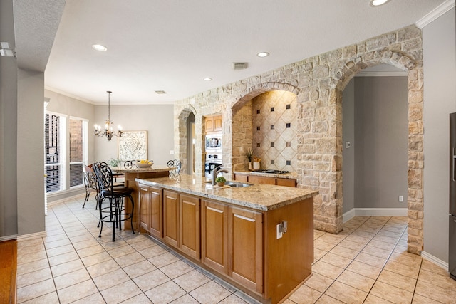 4607 Wellbrook Ln, Katy, TX 77450 - kitchen with stainless steel appliances, an island with sink, light tile patterned floors, light stone counters, and a chandelier
