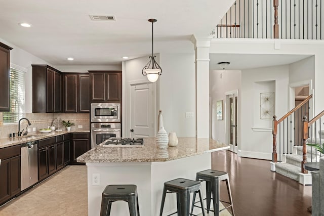 12102 N Founders Shore Dr, Cypress, TX 77433 - kitchen featuring stainless steel appliances, backsplash, light stone counters, dark brown cabinetry, and a breakfast bar