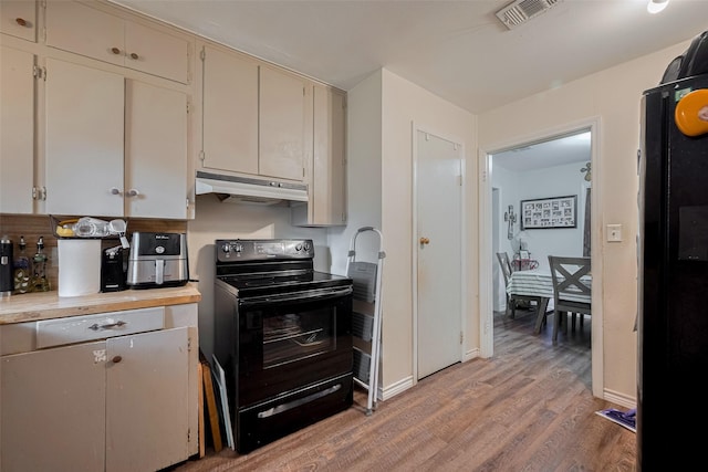 513 Frankie St, Wharton, TX 77488 - kitchen featuring black appliances, under cabinet range hood, light wood-style flooring, light countertops, and cream cabinetry