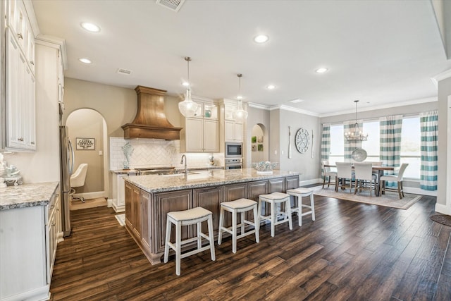 32319 Tall Oaks Way, Magnolia, TX 77354 - kitchen featuring custom range hood, arched walkways, appliances with stainless steel finishes, a large island, and dark wood-style flooring