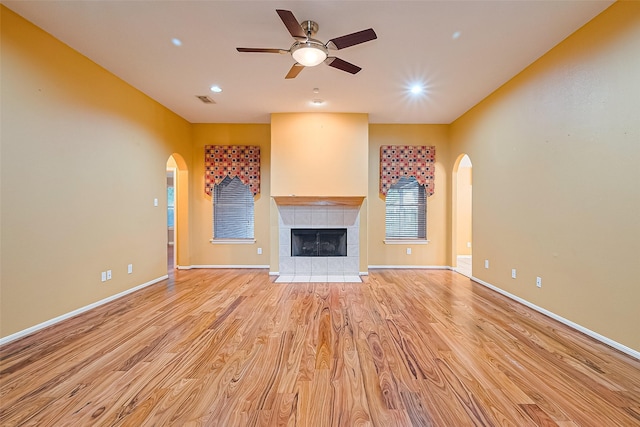 3803 Doveswood Cir, Needville, TX 77461 - unfurnished living room featuring arched walkways, light wood-style floors, ceiling fan, a tiled fireplace, and recessed lighting