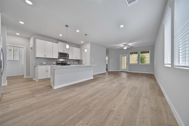 6609 Lahna Oak Dr, Conroe, TX 77304 - kitchen featuring stainless steel appliances, white cabinets, open floor plan, light wood-type flooring, and tasteful backsplash