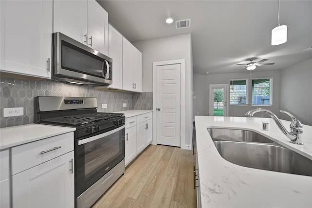 6609 Lahna Oak Dr, Conroe, TX 77304 - kitchen featuring stainless steel appliances, white cabinets, light wood-style floors, decorative backsplash, and ceiling fan