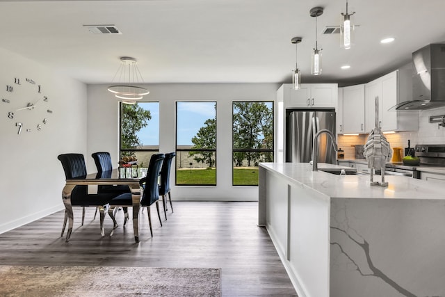 118 Hickory Pnes, Livingston, TX 77351 - kitchen featuring appliances with stainless steel finishes, wall chimney exhaust hood, backsplash, wood finished floors, and light stone counters