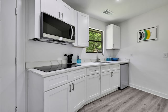118 Hickory Pnes, Livingston, TX 77351 - kitchen with black electric cooktop, light wood-type flooring, white cabinets, and light stone counters