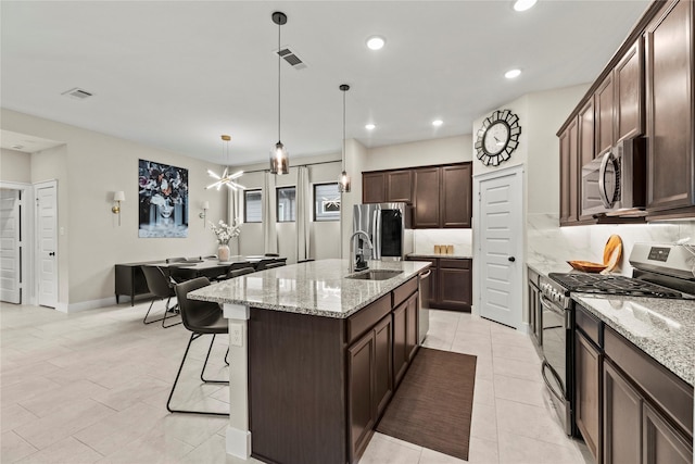 15247 Parkland Canyon Dr, Cypress, TX 77433 - kitchen with stainless steel appliances, dark brown cabinets, a kitchen island with sink, a breakfast bar, and decorative light fixtures