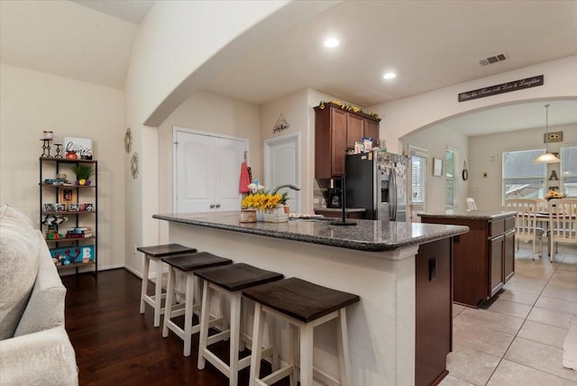 30119 Saw Oaks Dr, Magnolia, TX 77355 - kitchen featuring stainless steel fridge with ice dispenser, a center island with sink, arched walkways, dark stone counters, and recessed lighting
