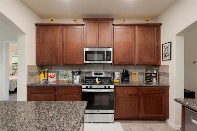 30119 Saw Oaks Dr, Magnolia, TX 77355 - kitchen featuring stainless steel appliances, tasteful backsplash, dark stone counters, brown cabinets, and light tile patterned floors