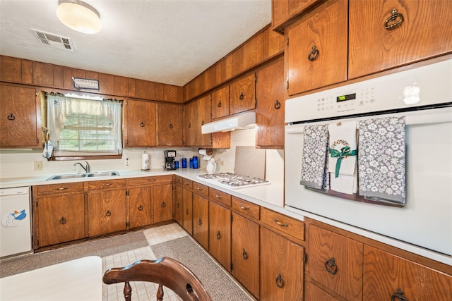 91 E Post Oak Ln, Shepherd, TX 77371 - kitchen with white appliances, under cabinet range hood, brown cabinets, and light countertops